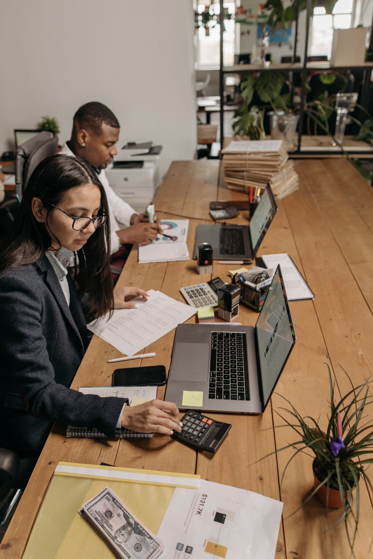 Two accountants working at a shared table with laptops and calculators