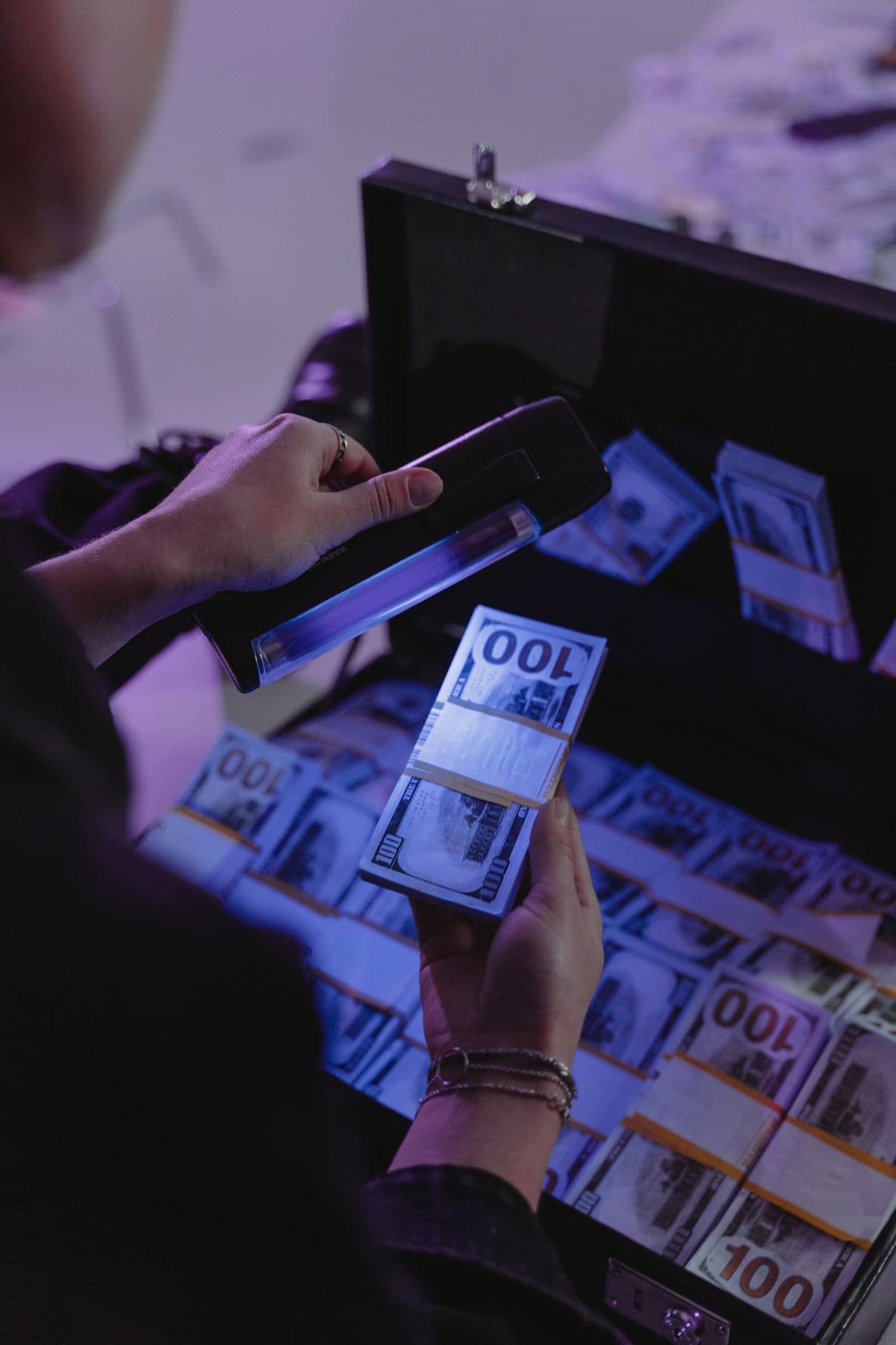 Person examining dollar bills under UV light for authenticity